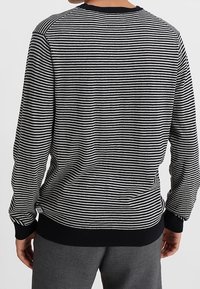 Maglione a strisce bianco e nero con maniche lunghe, colletto e polsini a coste, tessuto strutturato e vestibilità comoda, vista posteriore.