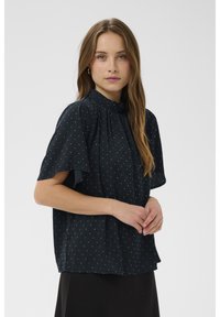 Blusa blu navy scuro con maniche corte a volant, pois bianchi e dettaglio arricciato sul collo, realizzata in tessuto leggero.