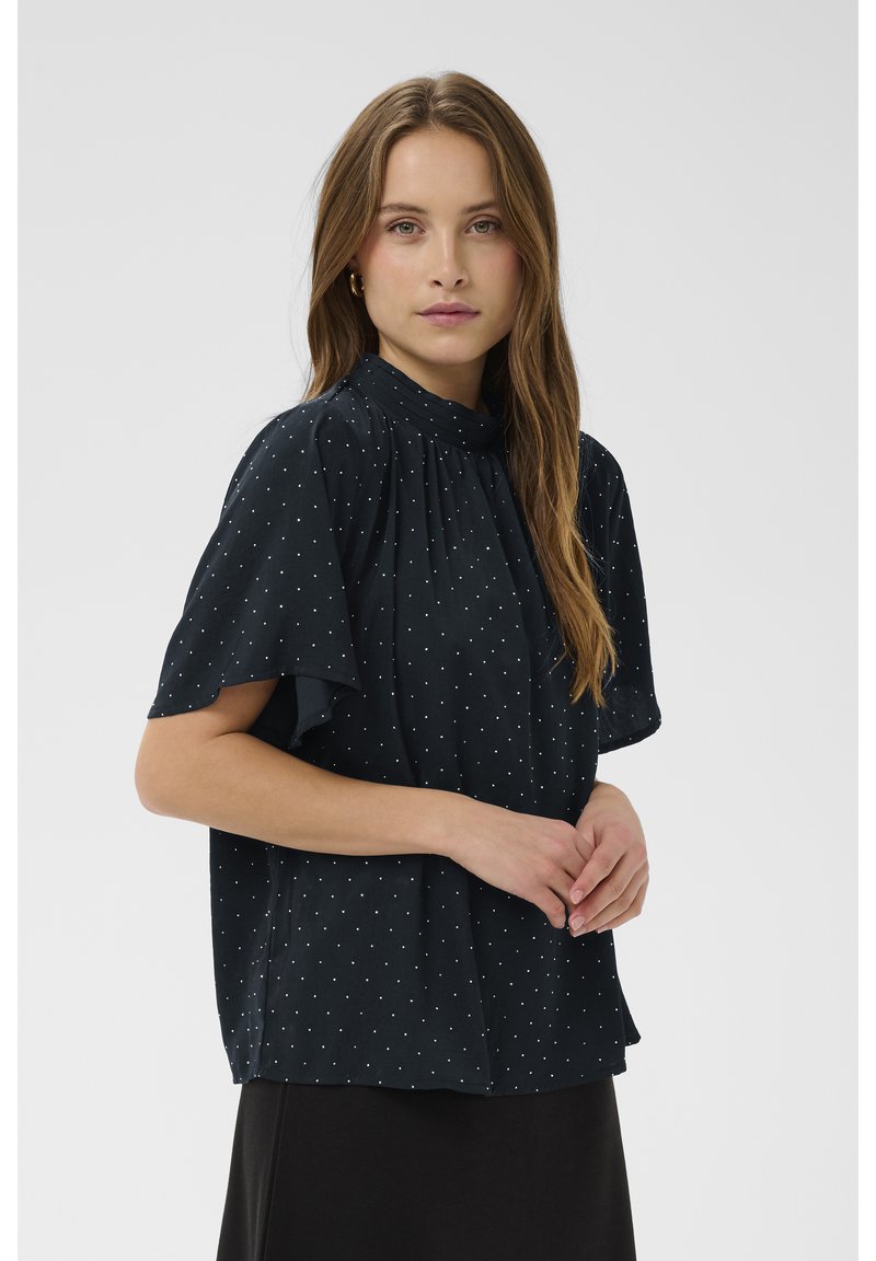 Blusa blu navy scuro con maniche corte a volant, pois bianchi e dettaglio arricciato sul collo, realizzata in tessuto leggero.