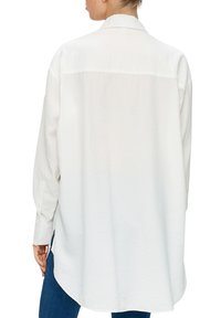White button-up shirt with a relaxed fit, long sleeves, and a rounded hem. Made from a soft, textured fabric.