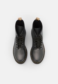 Botas negras con cordones, superficie texturizada, punta redonda y costuras amarillas a lo largo de la suela. Incluyen una lengüeta en el talón para facilitar su puesta.