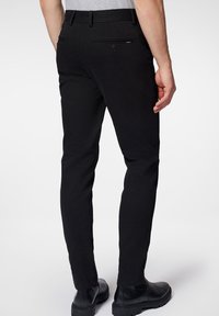 Czarne chinosy o slim fit, gładkim materiale, z szlufkami na pasek i tylnymi kieszeniami. Uzupełnione o czarne obuwie, które prezentuje się elegancko.