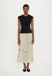 Top negru, ajustat, cu mânecă scurtă și față răsucită; asortat cu o fustă plisată, asimetrică, de culoare verde deschis; pantofi negri cu vârf ascuțit.