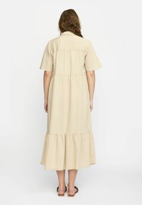 Beige midi-klänning med korta ärmar, strukturerad tyg, flerlagad volangnederdel och krage. Slät textur med vertikala ränder.