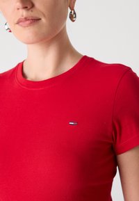 T-shirt en coton rouge avec un col rond, des manches courtes et un petit logo bleu, blanc et rouge sur la poitrine. Texture douce.