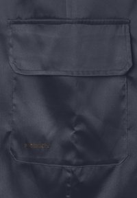 Tejido azul marino con un gran bolsillo tipo parche; el material tiene un ligero brillo. Un pequeño logo "FREDDY" en dorado es visible en el bolsillo.