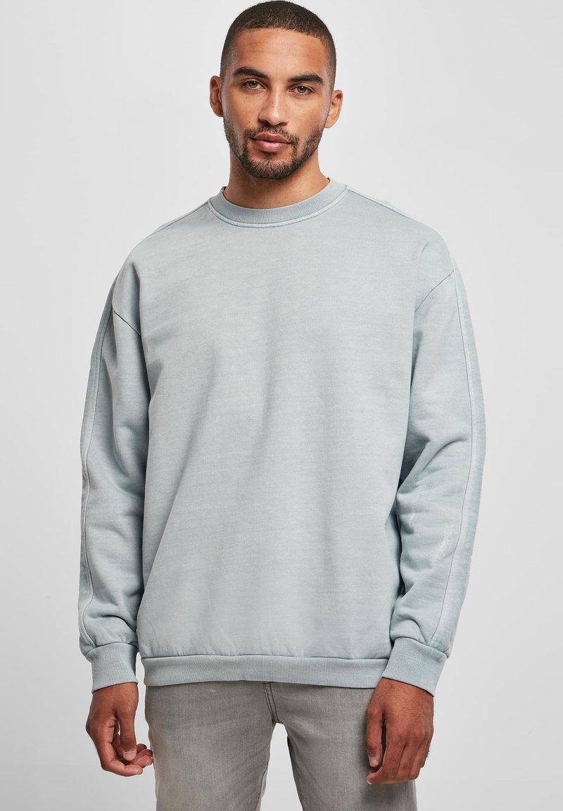 Felpa azzurro chiaro con scollo rotondo, maniche lunghe e polsini a costine. Texture liscia con una vestibilità ampia e un design sobrio.