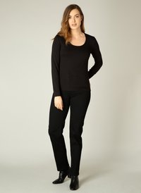 Zwarte top met lange mouwen en een ronde halslijn, gedragen met strakke zwarte broek en zwarte enkellaarzen, tegen een neutrale achtergrond.