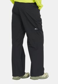Pantalons d'extérieur noirs avec une coupe décontractée, dotés de poches latérales, d'un branding discret sur la jambe droite et d'une texture de tissu lisse et léger.