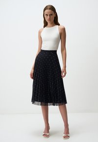 Gonna midi nera plissettata in chiffon, con motivi di stelle sparse in argento e blu. Abbinata a un top aderente bianco senza maniche.