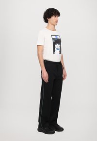 White t-shirt with graphic print featuring a face, paired with black pants with green side stripes. Model wears black sneakers.