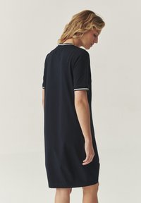 Robe bleu marine à manches courtes avec une coupe décontractée, présentant des accents blancs sur le col et les manches. Texture lisse, longueur au genou.