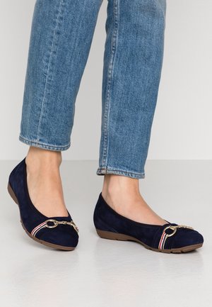 Granatowe baletki zamszowe z zaokrąglonym noskiem, złotym łańcuszkiem i akcentami w czerwono-białe paski, zestawione z jasnoniebieskimi podwiniętymi jeansami.