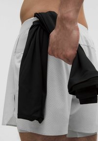 Weiße Sportshorts mit einer perforierten Textur, gehalten in der Hand zusammen mit einem schwarzen Shirt. Die Shorts besitzen einen Kordelzugbund.