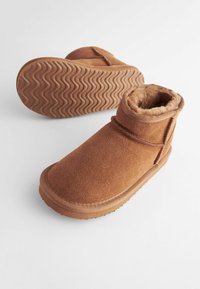 Bottines en daim marron avec une doublure douce et duveteuse et une semelle en caoutchouc striée. Présente un design simple avec un détail de bandage unique.