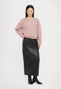 Gonna lunga nera in pelle abbinata a una felpa corta color rosa chiaro con orlo arricciato. La modella indossa stivali neri con tacco.