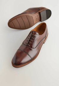 Brązowe skórzane buty eleganckie z okrągłym czubkiem, sznurowadłami i subtelnymi detalami przeszyć. Gumowa podeszwa z teksturowanym uchwytem i gładkim wykończeniem.