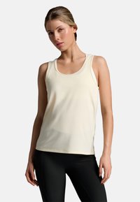 Top a canotta di colore crema chiaro con scollatura a U, realizzato in tessuto morbido e elasticizzato, abbinato a leggings neri attillati. Logo del marchio discreto all'orlo.