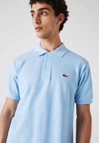 Polo shirt bleu clair en tissu respirant, avec un col et des manches courtes. Logo brodé sur la poitrine gauche. Coupe classique.
