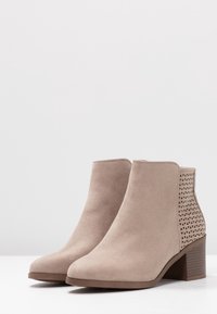Beige nilkkurit pehmeästä mokasta, joissa on geometrinen leikattu muotoilu kantapäässä ja kohtuullinen lohkarekorko.