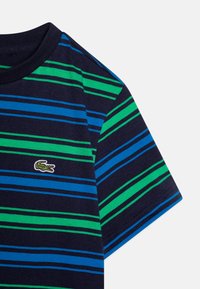 T-shirt rayé avec des lignes horizontales en bleu marine, vert et bleu. Manches courtes avec un col rond et logo brodé sur la poitrine.