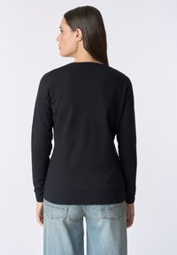 Maglione nero lavorato a maglia con maniche lunghe e scollatura arrotondata, presenta una superficie liscia e orlo a costine. Indossato con jeans blu chiaro.