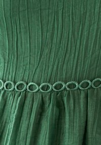 Grünes Kleid aus einem strukturierten, zerknitterten Stoff. Mit einer dekorativen, geschlungenen Borte in passendem Grün entlang der Taille.