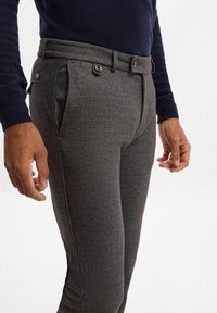 Graue gewobene Hose mit maßgeschneidertem Schnitt, ausgestattet mit vorderen Falten, Knopfdetails, seitlichen Taschen und einer glatten Textur.