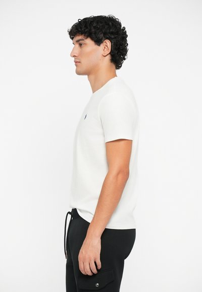 Tricou alb din bumbac, cu mâneci scurte, decolteu rotund și un mic logo albastru pe piept, asortat cu pantaloni negri cu buzunare.