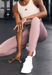 Světle růžové sportovní legíny s hladkou texturou a ozdobným švem, spárované s béžovým crop topem s černým logem a bílými teniskami.