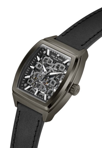 Quadratische Uhr mit schwarzem Lederarmband, metallgrauem Gehäuse und transparentem Ziffernblatt, das die inneren Mechanismen zeigt, mit stilisierten Stundenmarkierungen.