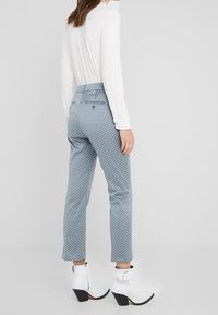 Blauwe geprinte broek met een slim fit, voorzien van een hoge taille en een geometrisch ontwerp, gecombineerd met witte enkelboots.
