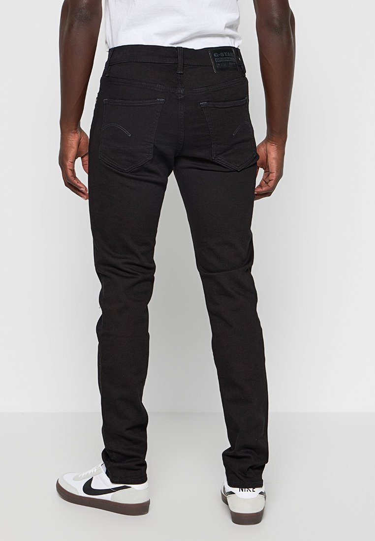 Jean slim noir en denim, doté de deux poches arrière, d'une étiquette logo à la taille et d'un minimalisme dans les détails de couture.