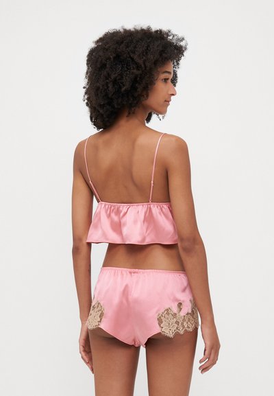 Set da loungewear in satin rosa composto da due pezzi, con top corto arricciato e pantaloni corti con accenti di pizzo sui lati. Texture liscia, design casual.