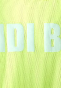 Tessuto di rete giallo con grandi lettere bianche parziali "ADI B" stampate su di esso, probabilmente parte di una parola o un nome di un marchio su un indumento.
