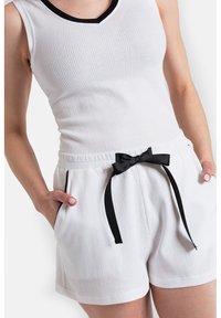 Biały, pleciony top na ramiączkach z czarnym dekoltem, zestawiony z białymi szortami o strukturze i czarną kokardą do ściągania w pasie.