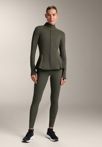 Olive green athletic jacket with a high collar and full zipper, paired with matching leggings. Lightweight, fitted fabric with minimal seams.