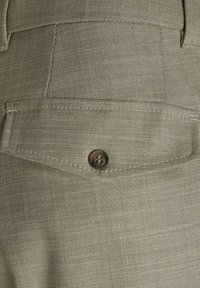 Tissu beige avec un tissage texturé, présentant une poche arrière de forme arrondie, fermée par un bouton rond marron.