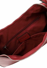 Interno di una borsa in pelle bordeaux con una tasca con zip e rivestimento in tessuto, dettagli in metallo argentato sulla zip e un'etichetta testurizzata.