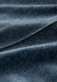 Selymes textúrájú farmeranyag halszálka mintával, sötétkék és világosabb kék szálakkal, hajtogatott redőkkel.