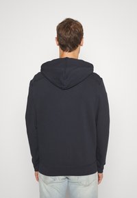 Sudadera azul marino con capucha, de ajuste relajado, mangas largas y un diseño sencillo. Textura suave sin patrones visibles ni elementos metálicos.