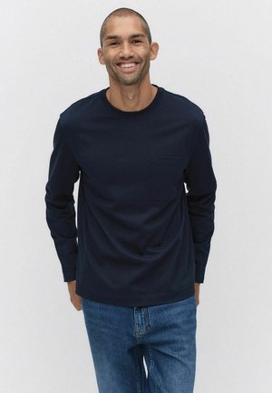 Navy long-sleeve shirt with a round neckline and a chest pocket, paired with light blue denim jeans. Smooth fabric texture.