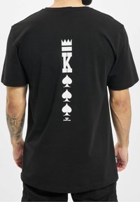 Sort bomulds T-shirt med stort hvidt trykt design på ryggen, herunder spade symboler og teksten "KING OF COMPTON."