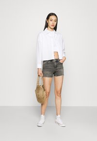 Chemise blanche à manches courtes et boutonnée, shorts en denim gris, baskets blanches et sac rond tressé. Texture lisse, design décontracté, palette de couleurs claire.