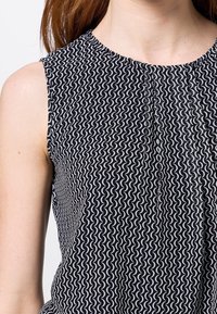 Top sans manches noir et blanc avec un motif ondulé, décolleté rond et plis subtils au centre, fabriqué en tissu léger.