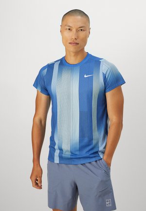 Nike sinine spordipüksi lühikeste varrukatega särk, millel on gradueeritud ruuduline muster ja logo, koos heleda halli lühikesed püksid.
