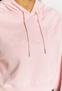 Sudadera rosa claro de algodón, con un logo de Puma bordado en blanco. Tiene una capucha con cordón y un dobladillo acanalado para un ajuste ceñido.