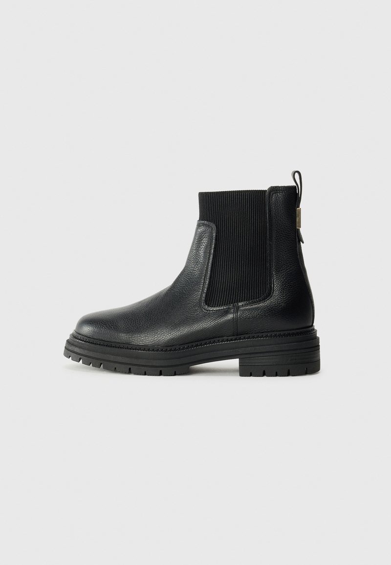 Bottine en cuir noir avec panneau latéral élastique côtelé, languette à l'arrière et semelle épaisse texturée, montrée de profil sur fond uni.