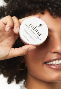 Rahua Smoothing Hair Balm in einem runden weißen Behälter mit schwarzem Text. Der Deckel zeigt ein grafisches Design. Der Behälter wird von einer Hand gehalten.
