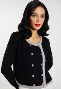Zwarte gecropte cardigan met zilverkleurige knopen en grijze accenten, met een ronde halslijn en een zachte, gestructureerde stof.